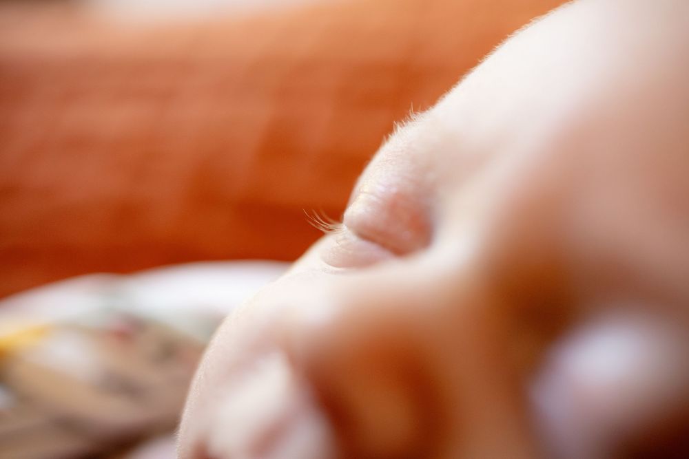 Extreme close-up of a newborn baby's tiny fingers with fine hairs against a soft, blurred orange background.