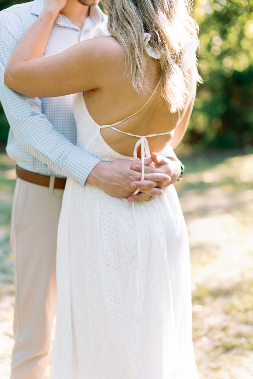 Close-up of couple embracing outdoors, showcasing open-back tie detail of woman's white eyelet wedding dress.