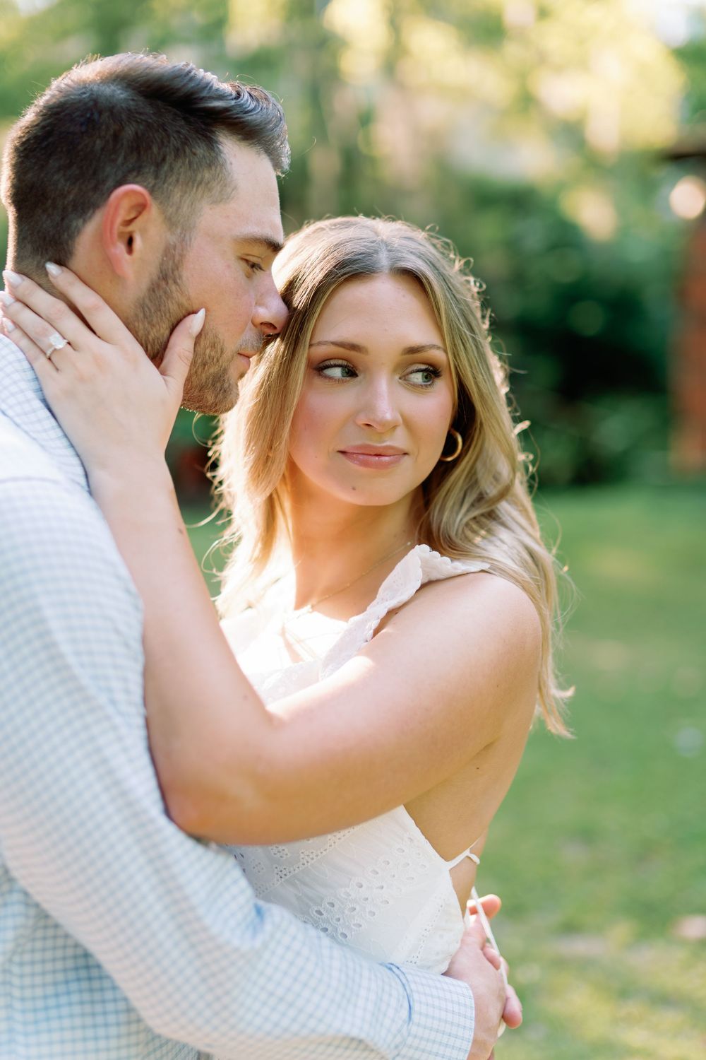 Engaged couple in soft golden light, man kissing woman's cheek as she smiles wearing a diamond engagement ring.