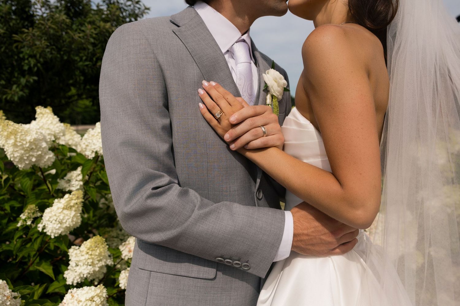 Bride and groom sharing a kiss outdoors, with white hydrangeas in the background during their wedding ceremony.
