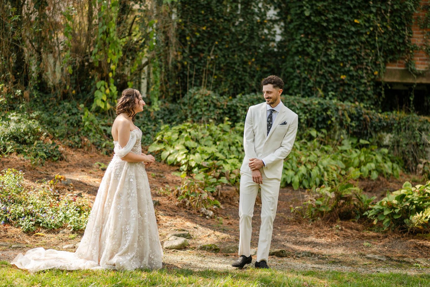 Groom smiles joyfully at bride during first look moment in lush green garden setting.