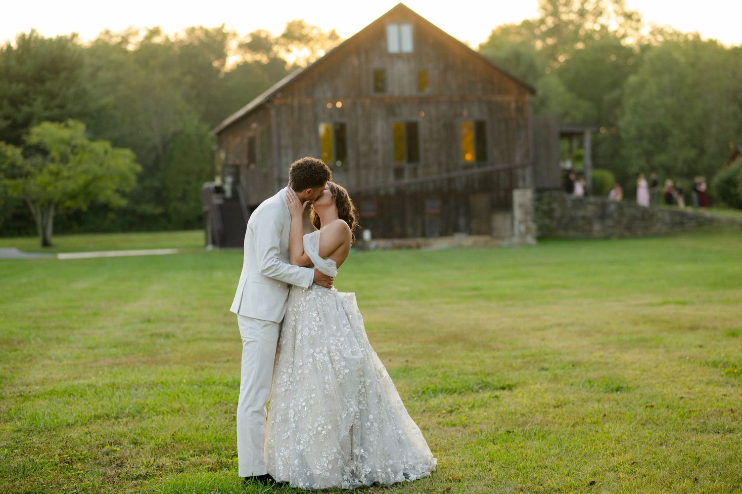 Couple shares a romantic kiss in front of a rustic barn at golden hour sunset.