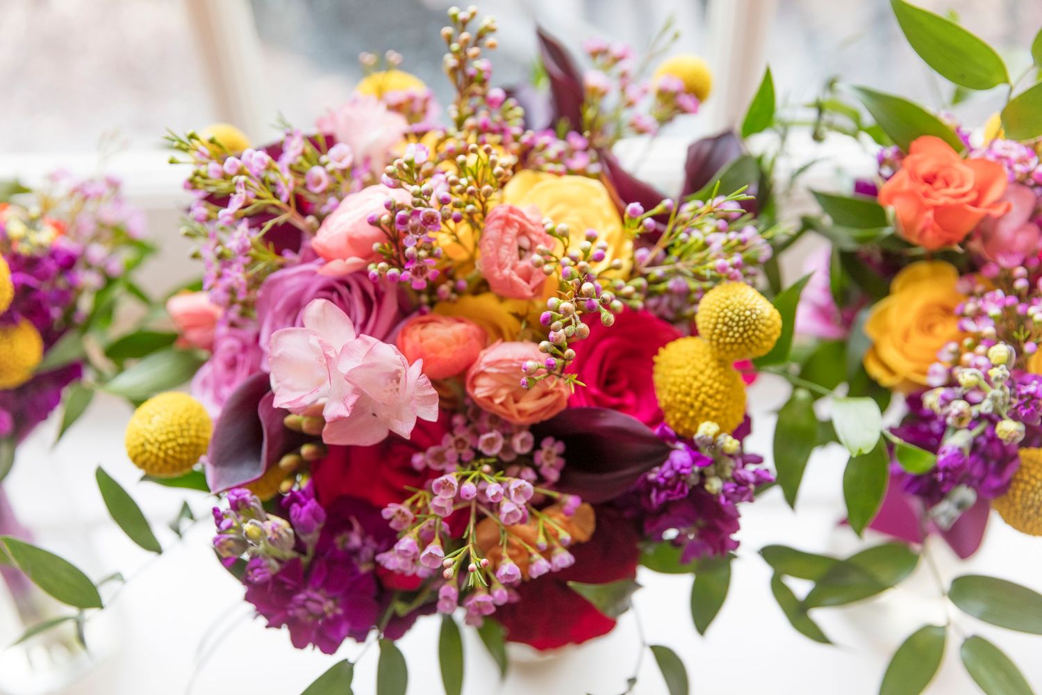 Vibrant wedding bouquet with pink, yellow and purple flowers arranged with greenery.