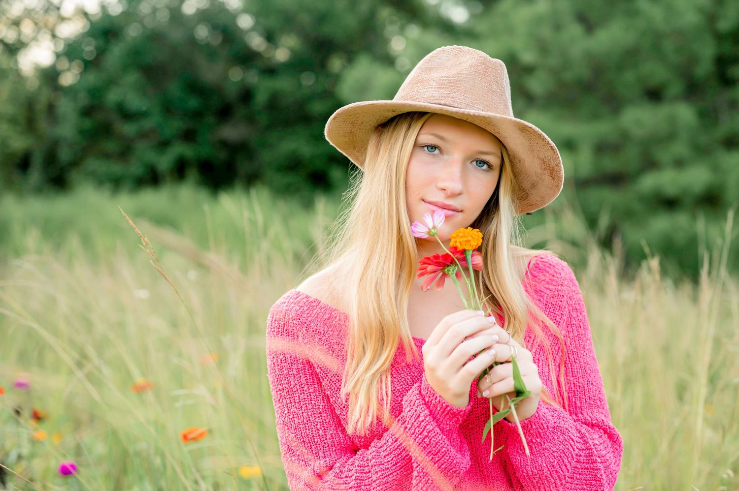 A summer portrait featuring a pink sweater, straw hat, and bright orange flower in a meadow setting.