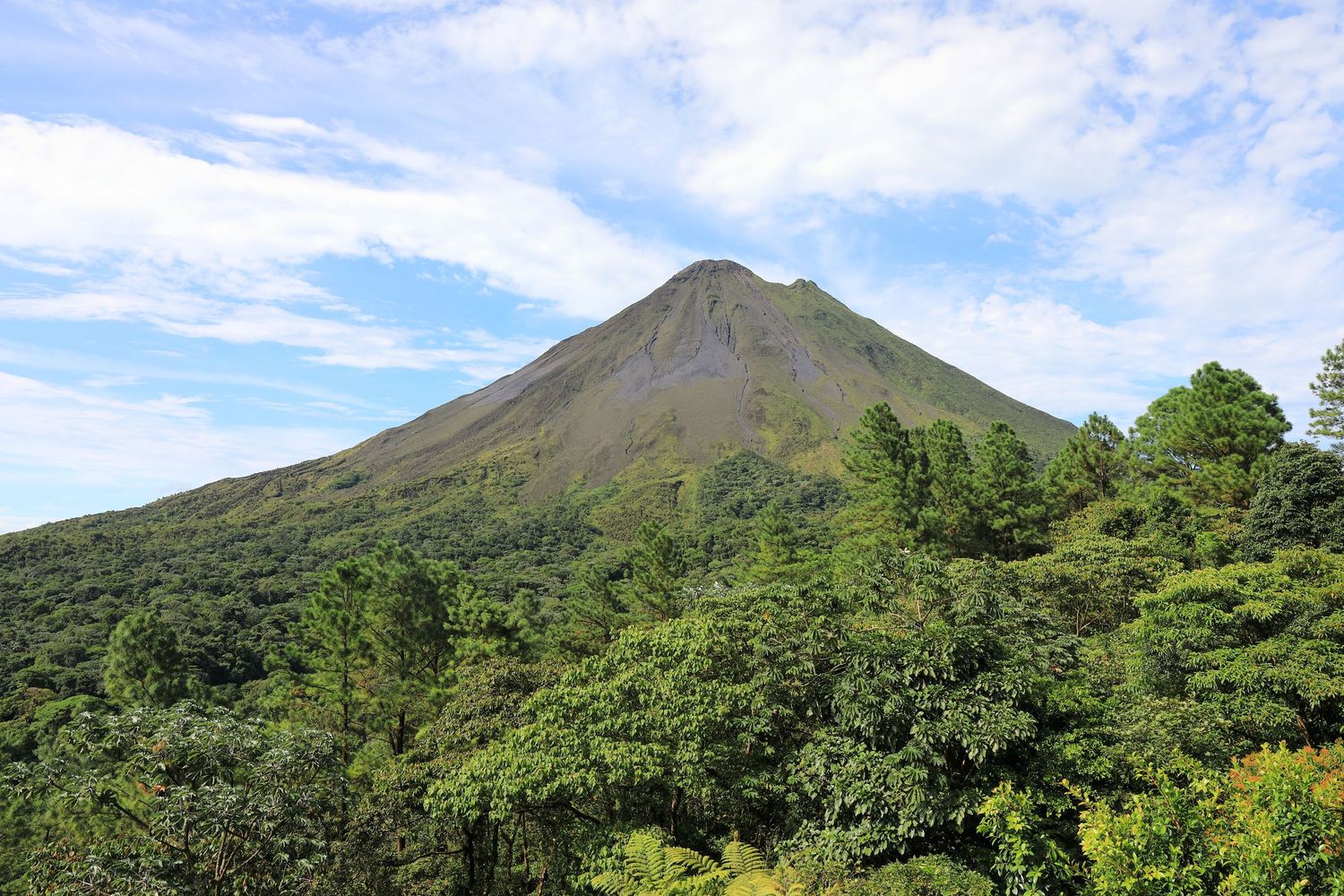 Arenal Volcano rises above the green forest landscape under blue skies.