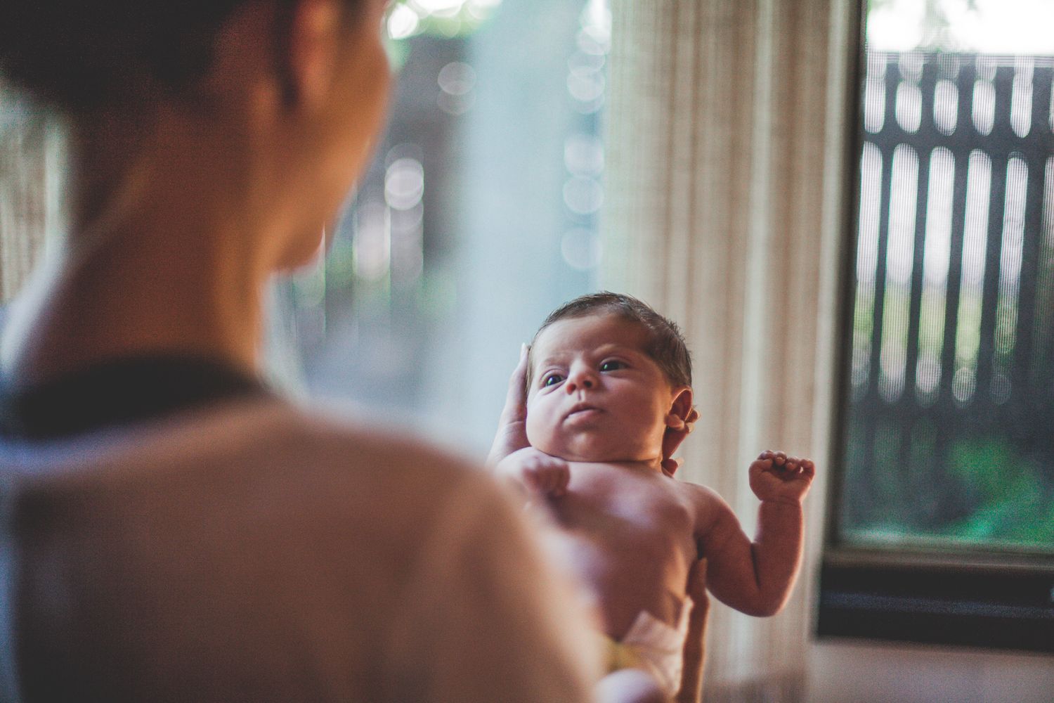 A mother holds her newborn baby near a bright window in a tender moment.