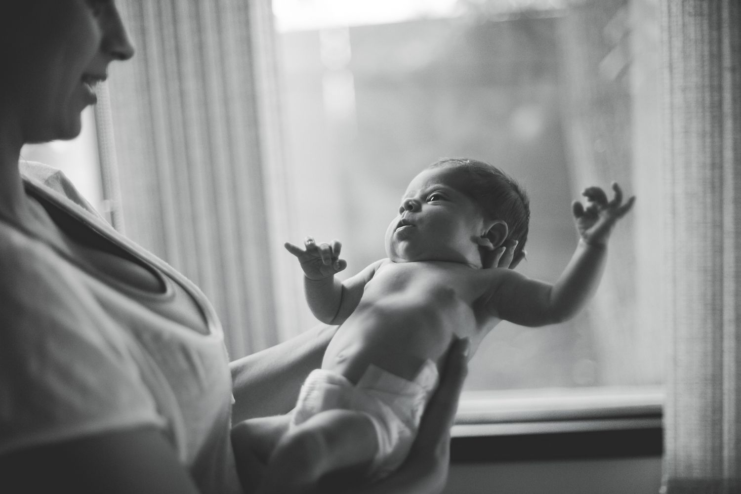 Black and white photo of a mother gently holding her newborn baby near a window.