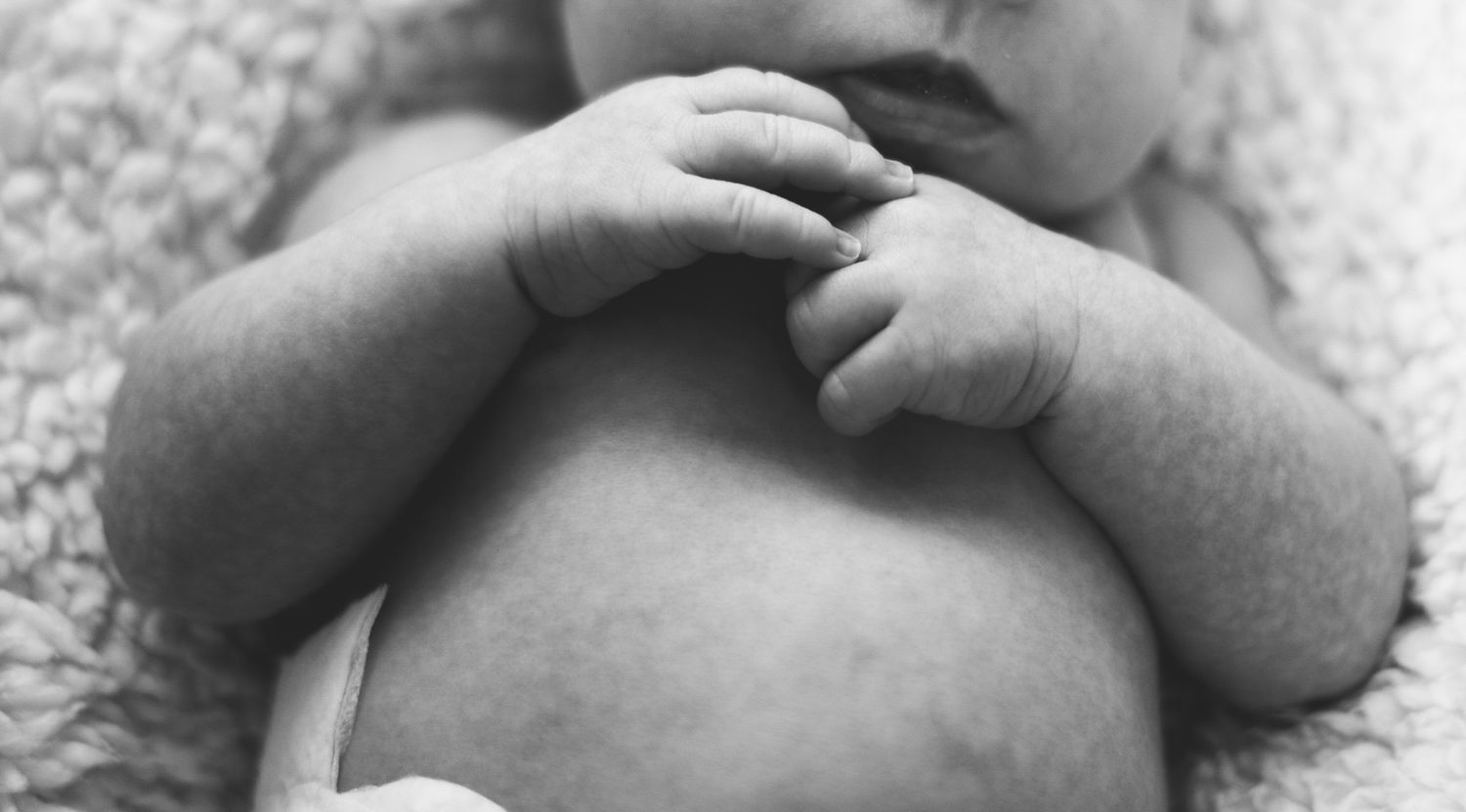 Close-up black and white photo of a newborn babys tiny hands resting on their chest.