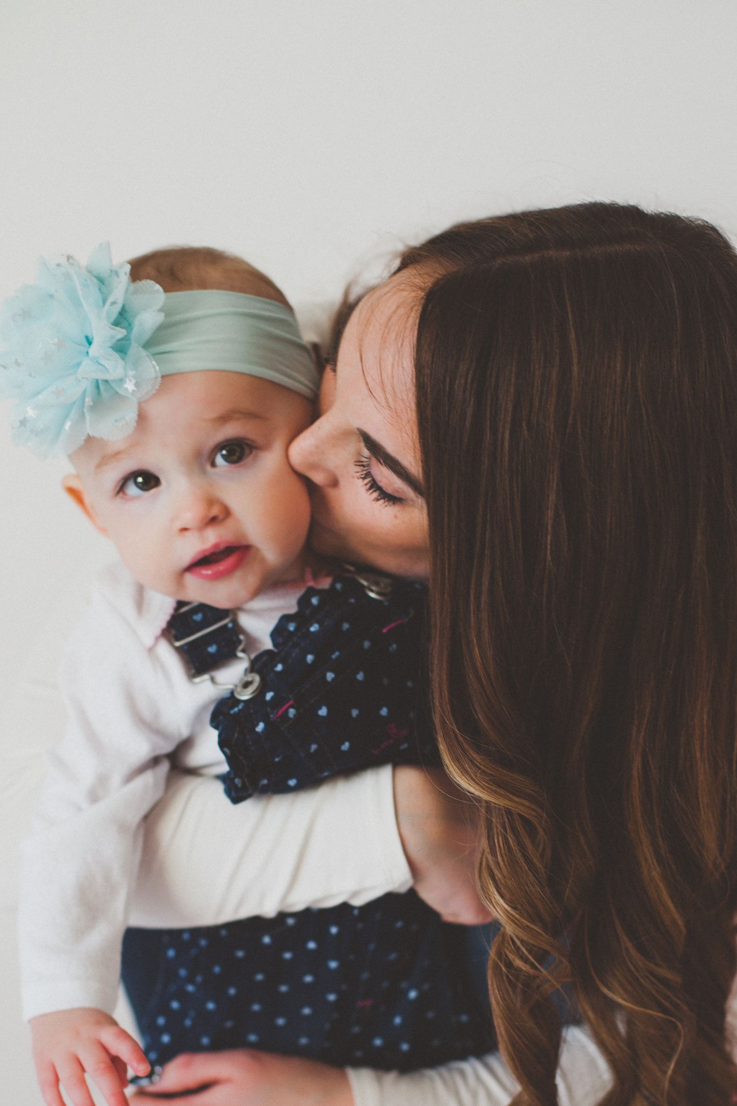 A tender moment as a brunette mother kisses her baby wearing a teal floral headband.