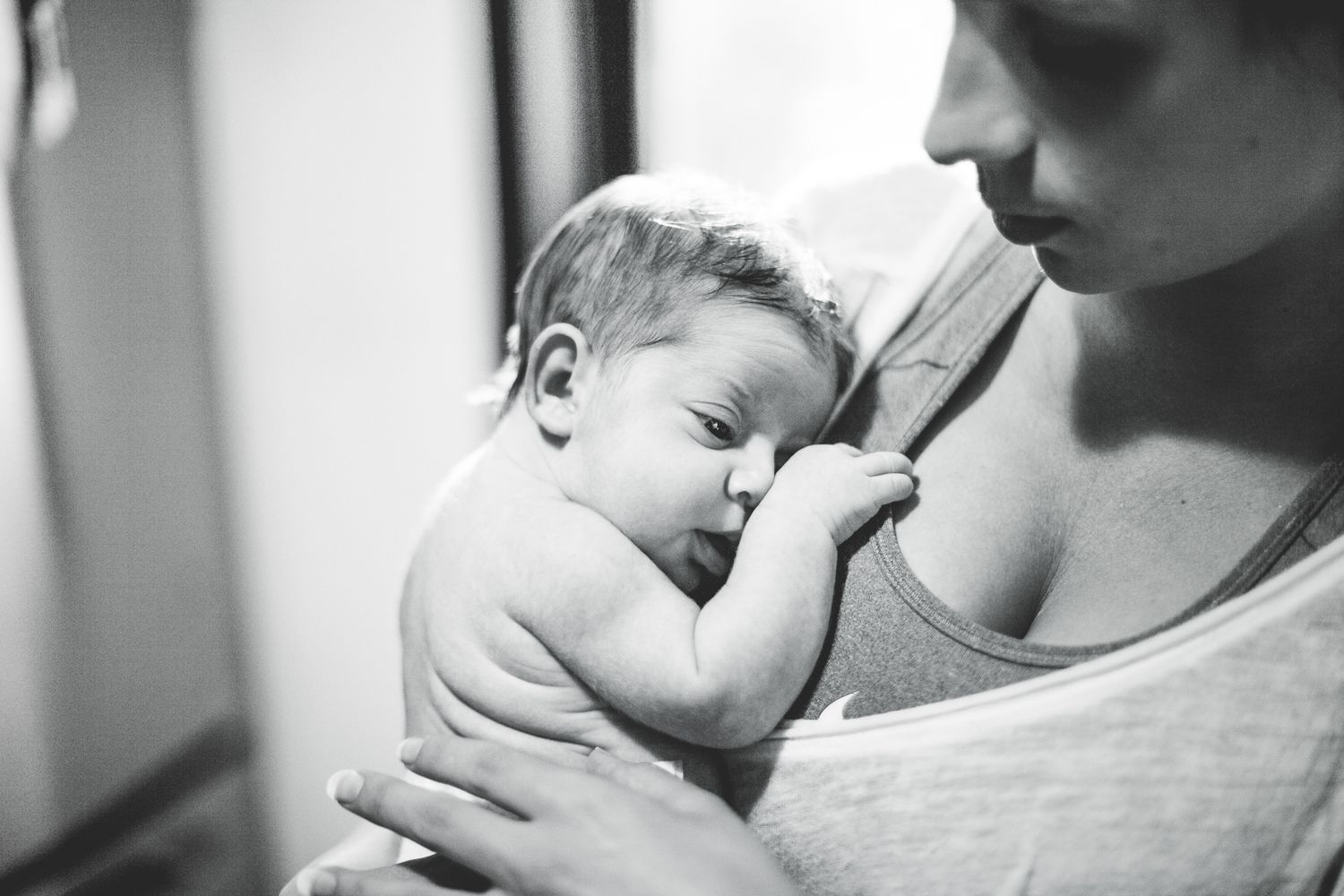 A mother tenderly holds her sleeping newborn baby close to her chest in a black and white photo.