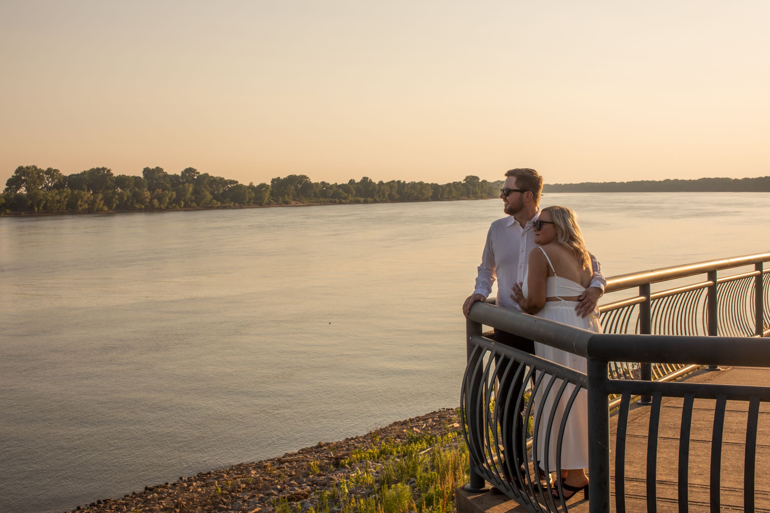 A couple shares an intimate sunset moment overlooking a serene waterfront.