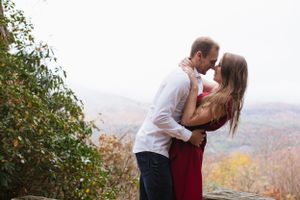 Romantic couple in red dress and white shirt embrace on mountain overlook in autumn.