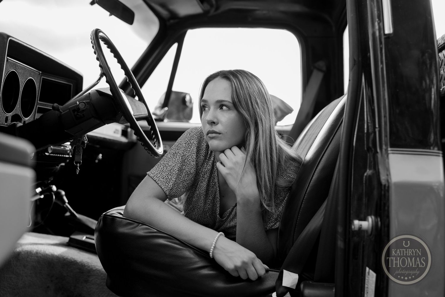 A black and white portrait of someone sitting in a vintage vehicle interior.