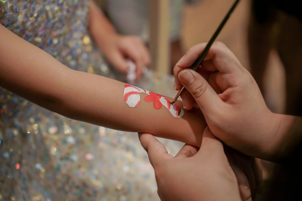 Close-up shot of hands carefully painting decorative art on someone's arm at a party.