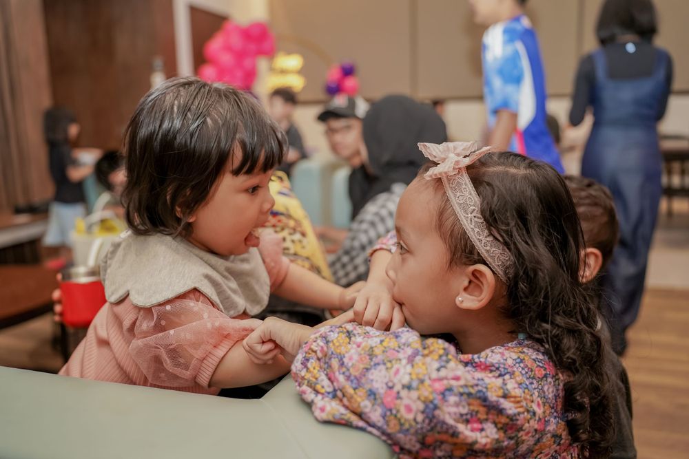 Two children in pink dresses chatting at indoor celebration event.