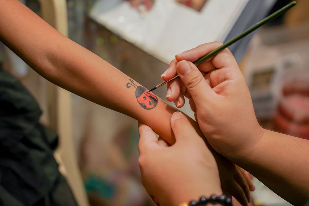 Close-up of hands painting temporary art on someone's arm during a party.