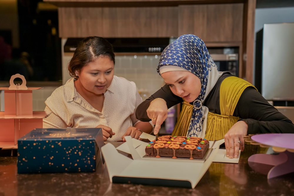 Two people examining items on wooden table during indoor celebration.