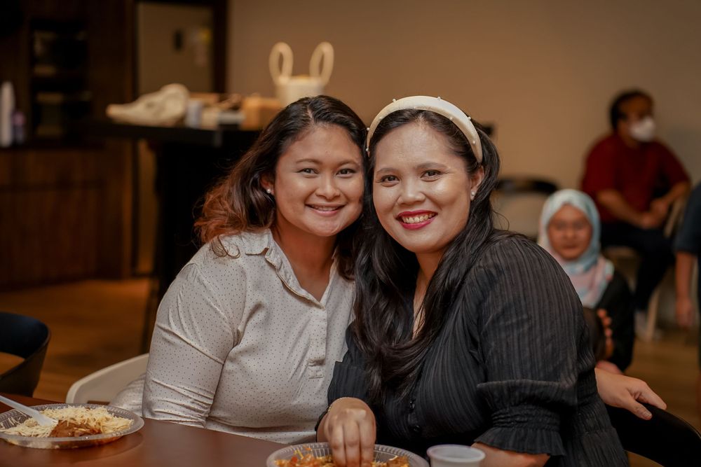 Two friends smiling warmly together at a casual indoor gathering.