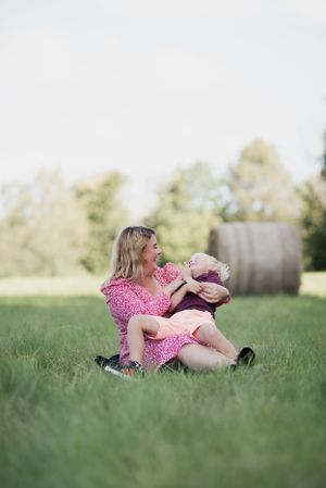 A sweet moment captured in a grassy field with pink floral dress and hay bales visible in the background.