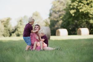 Tender family moment in a sunlit field with round hay bales in the background.