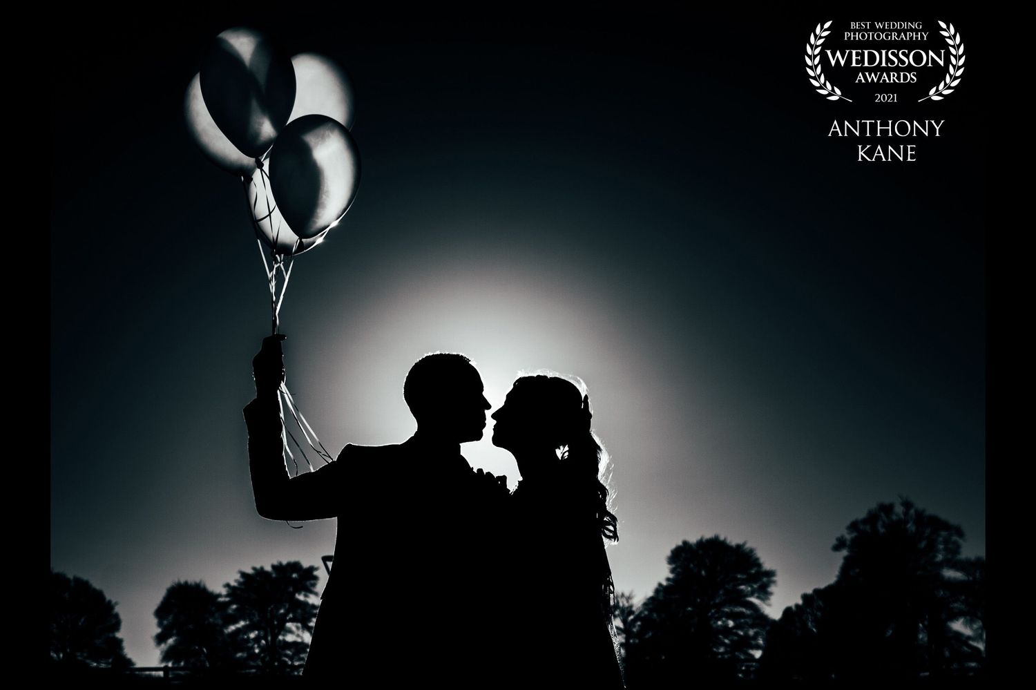 Silhouette of a couple with balloons against a backlit sky creating a romantic mood in the Phoenix Park.