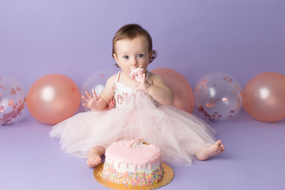 Baby in pink tulle dress with cake and balloons during first birthday photoshoot.