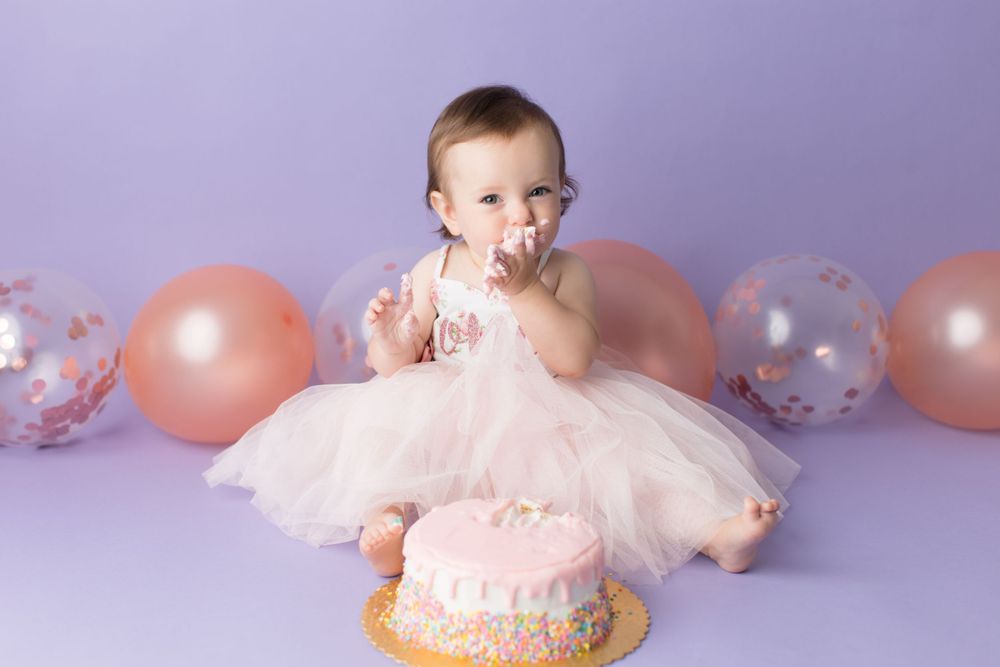 Baby tastes frosting from pink birthday cake during cake smash photo session.