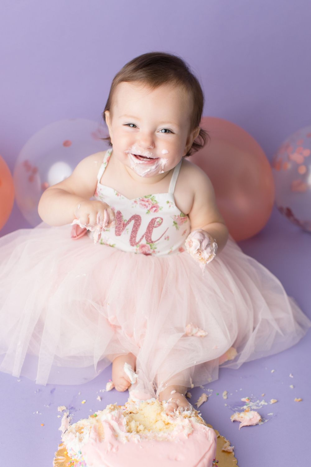 Baby covered in cake frosting smiles during festive cake smash photography session.