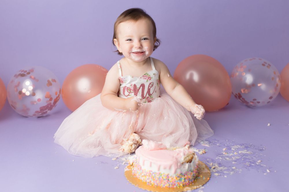 First birthday celebration with pink cake smash session against purple background with balloons.