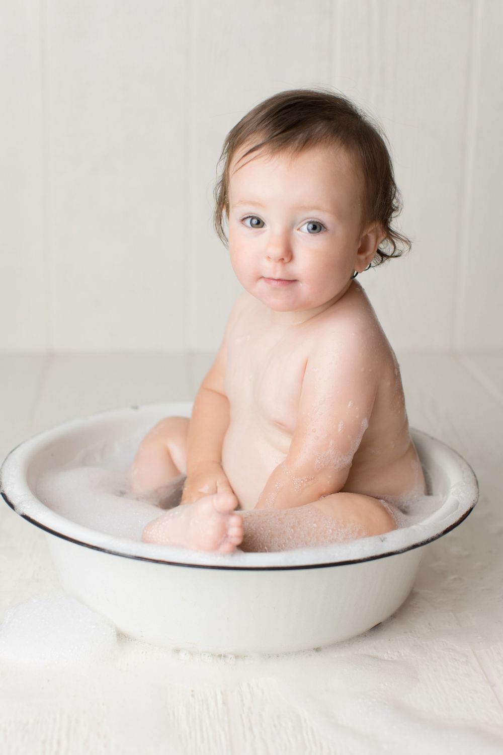 Bath time portrait of infant sitting in vintage white enamel basin.