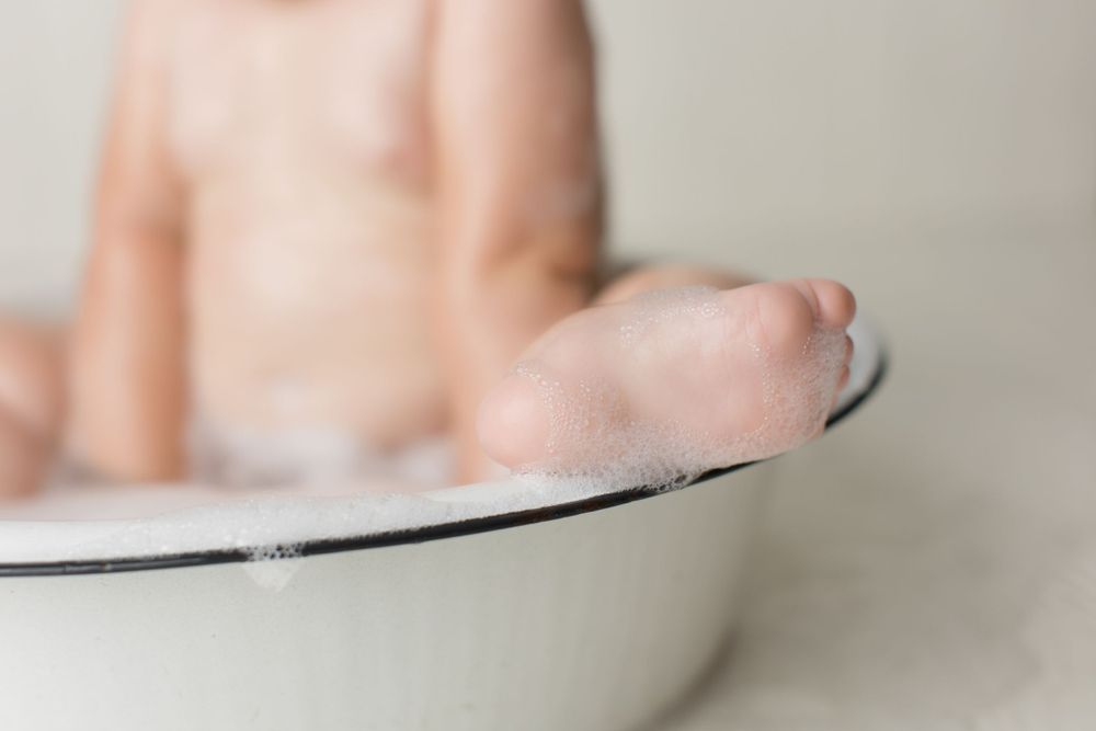Close-up detail of tiny feet resting on edge of vintage white enamel basin.