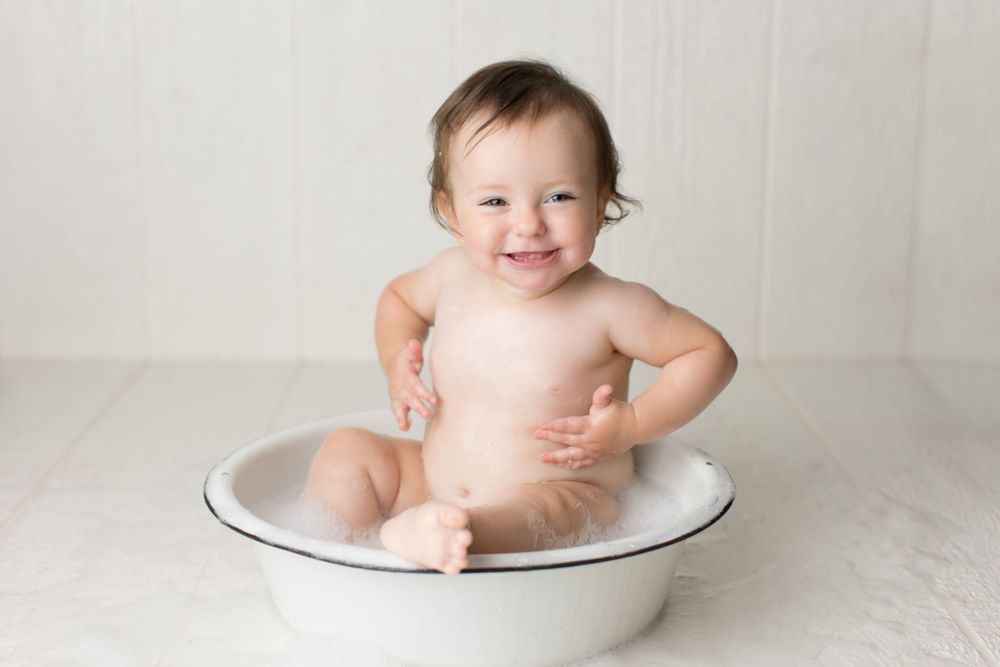 Happy bath time portrait in vintage white enamel basin against neutral backdrop.