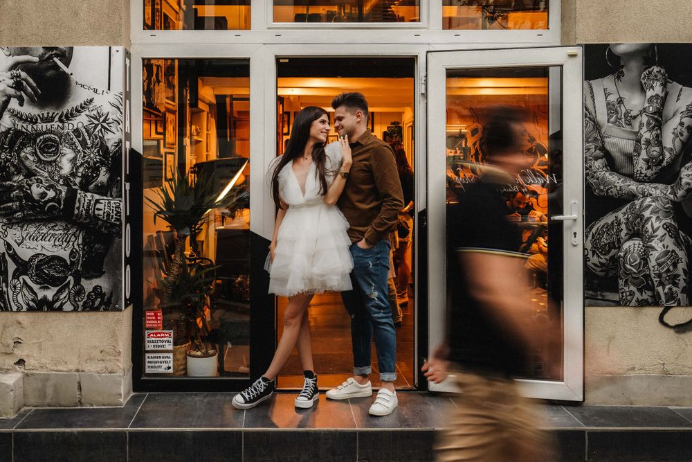 Couple posing in doorway of illuminated storefront with artistic murals.