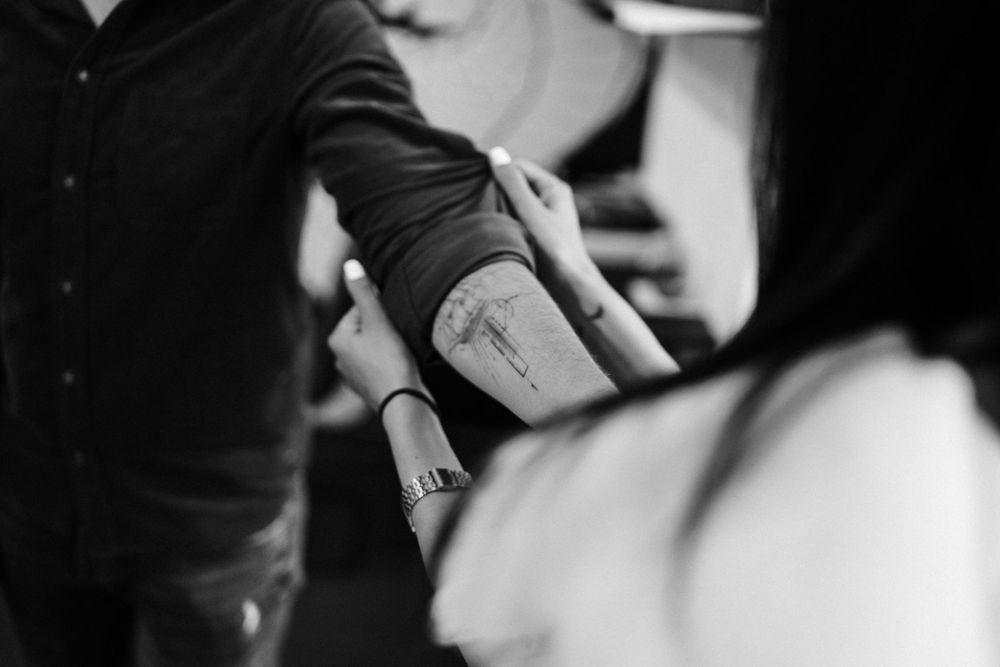 Close up of two people showing matching tattoos on their arms.
