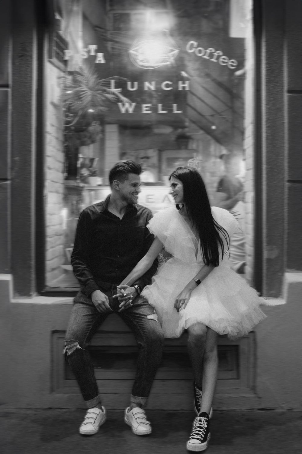 Black and white photo of couple sitting outside cafe window with 'Lunch Well' sign.