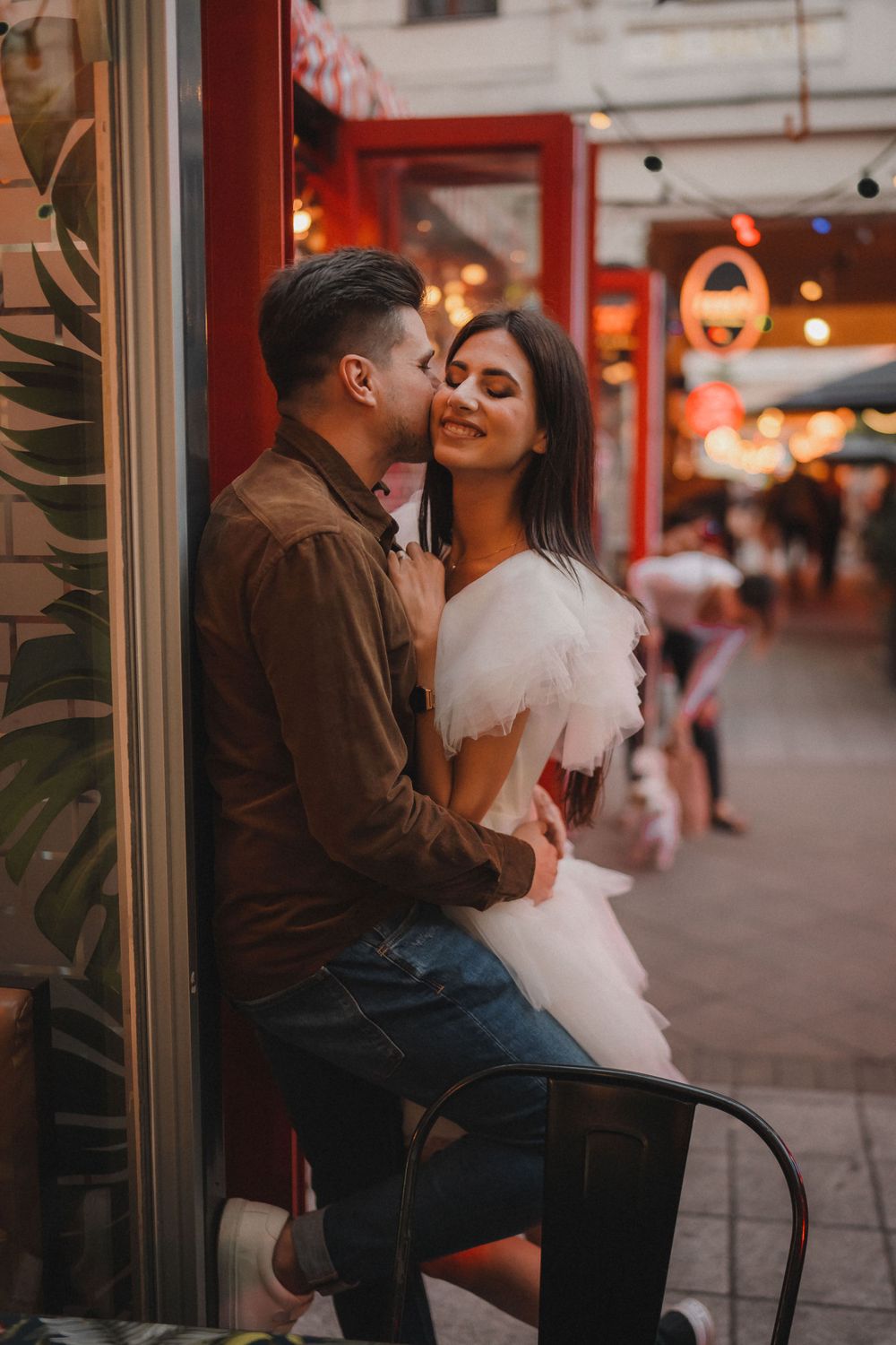 A tender moment captured outside a storefront with red accents and warm lighting.