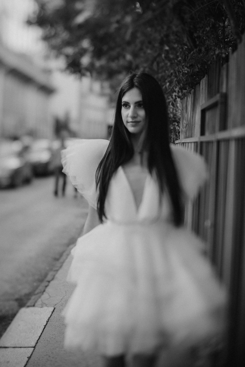 Dreamy black and white portrait in flowing white dress on city sidewalk.