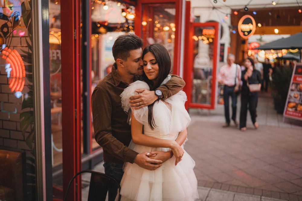 A tender embrace outside storefronts with warm lighting and brick walls.