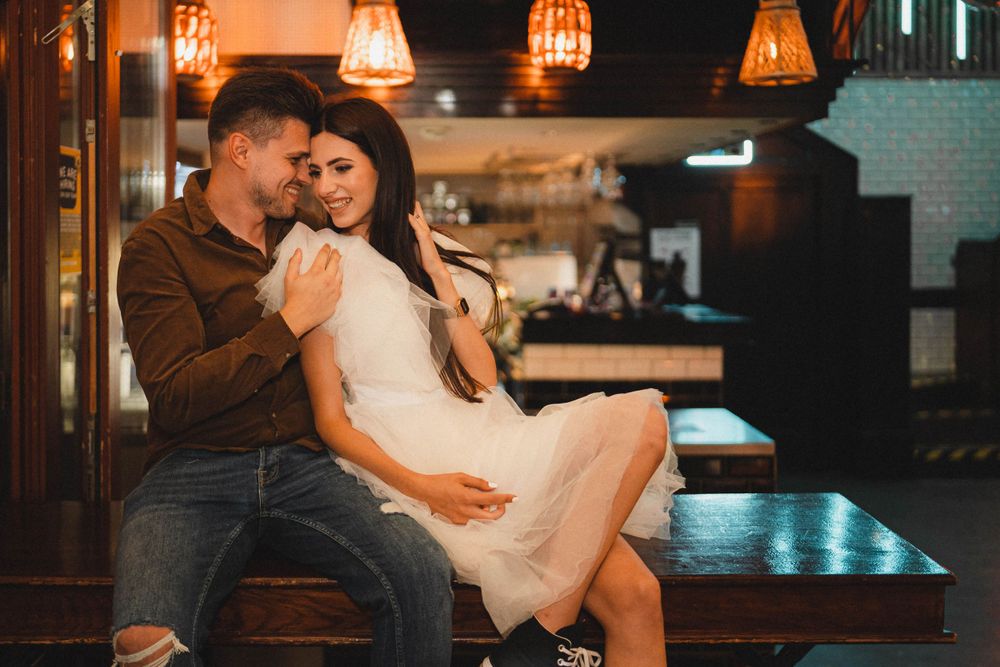 A romantic moment in a dimly lit bar setting with hanging pendant lights.