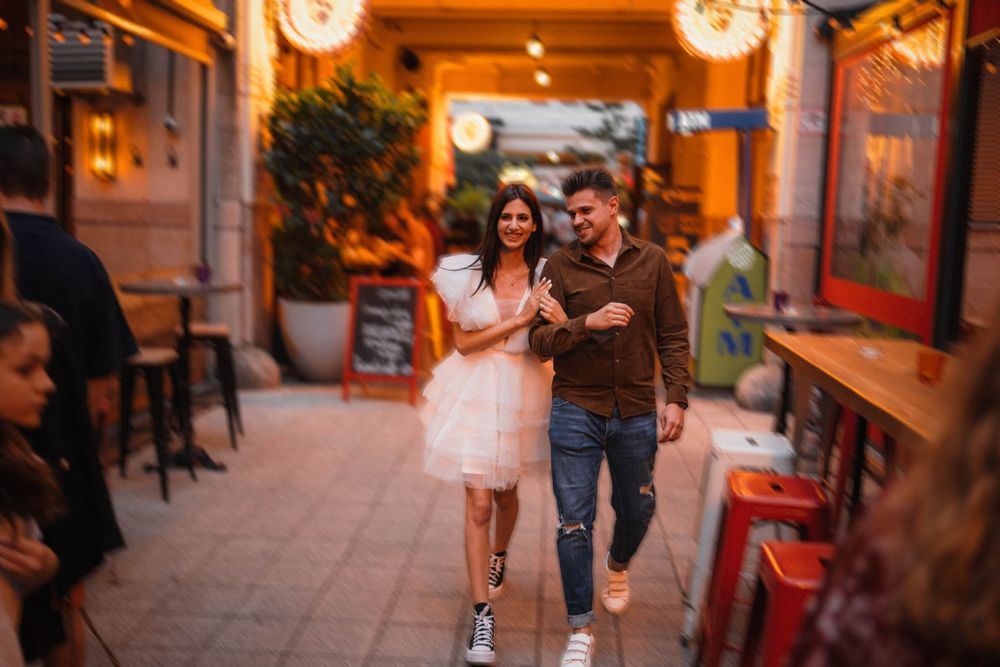 A couple walking through an illuminated restaurant corridor in casual evening attire.
