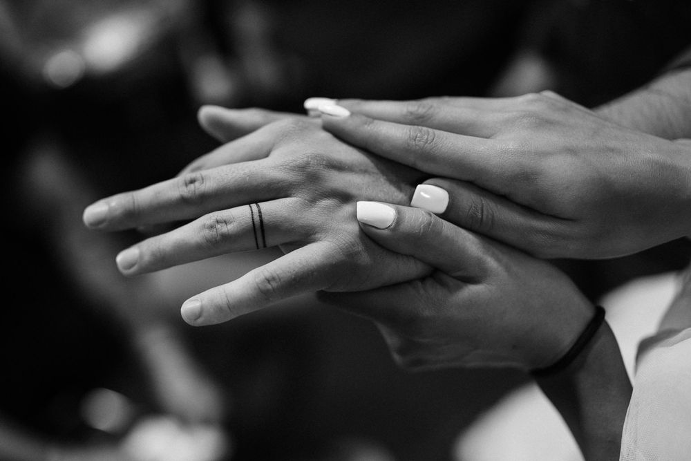 Black and white close-up of hands exchanging rings during intimate moment.