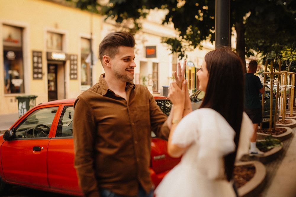 Couple having conversation on urban street next to red car at sunset.