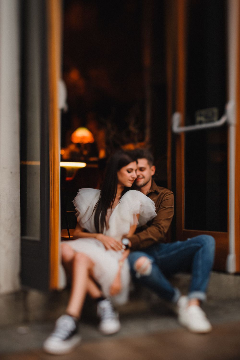 A couple shares an intimate moment while sitting in a doorway with warm lighting.