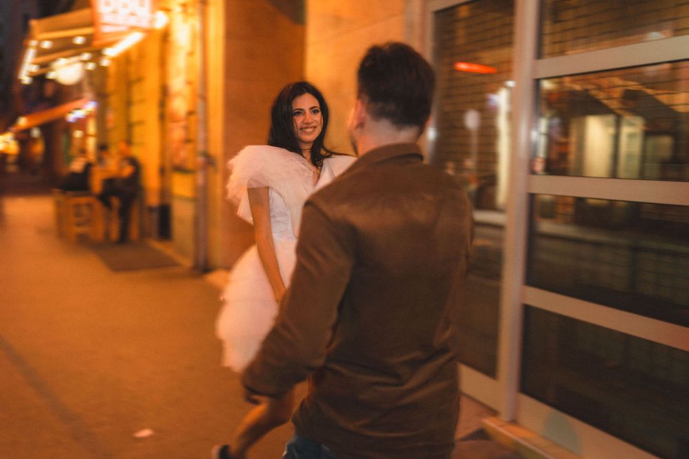 A couple playfully interacts on an evening city street with ambient lighting.
