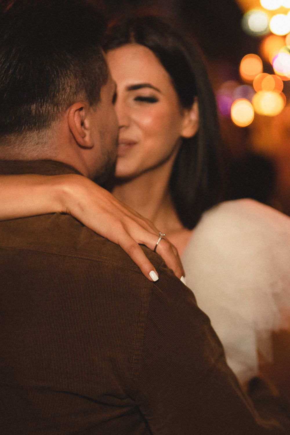 An intimate moment captured between a couple on a city street with bokeh lights in the background.