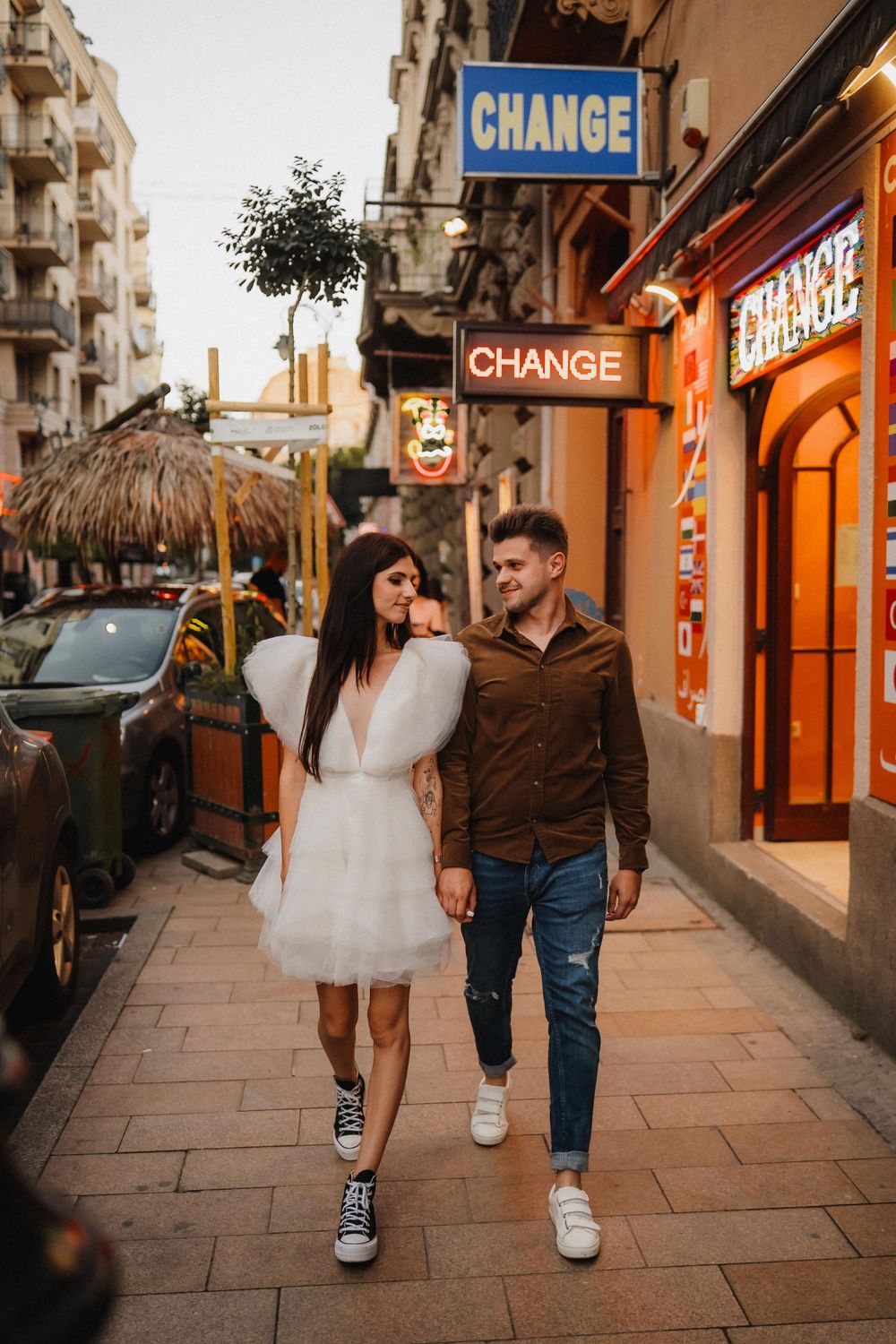 Couple strolling under Change sign on illuminated city street at dusk.
