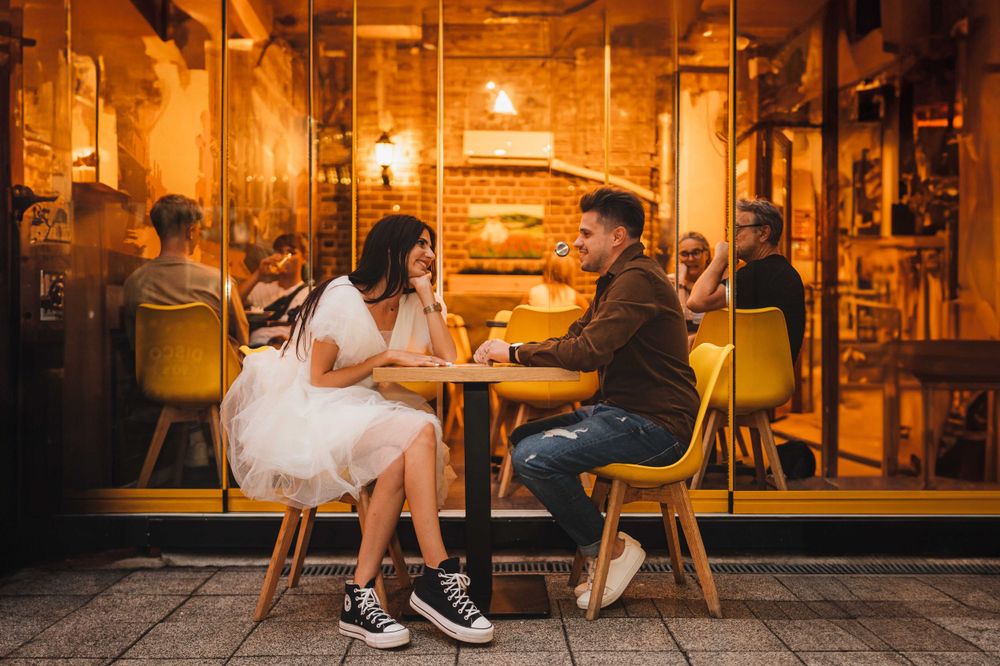 Couple sitting at warm glowing cafe table shares intimate conversation in cozy evening ambiance.