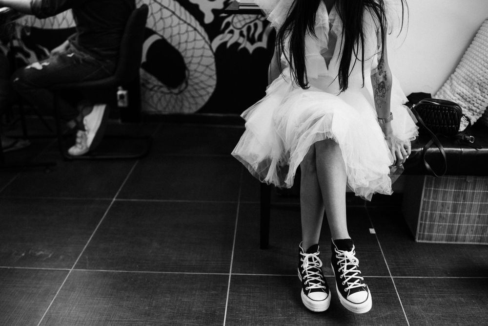 Close-up of legs wearing sneakers with tulle dress against dark tiled floor.