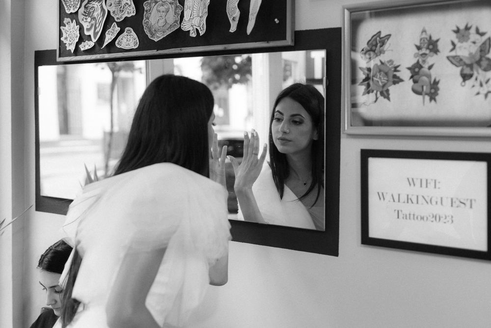 Person in white dress checking reflection in mirror with artwork on wall.