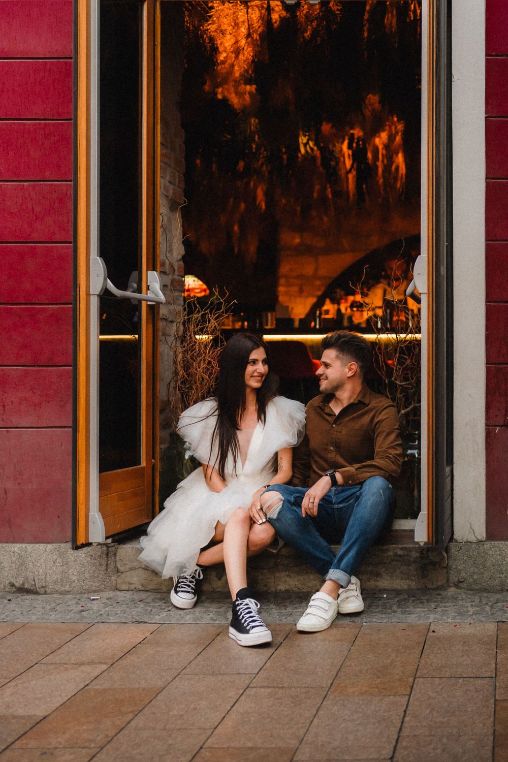 Couple sitting in doorway with warm orange lighting and red wall backdrop.